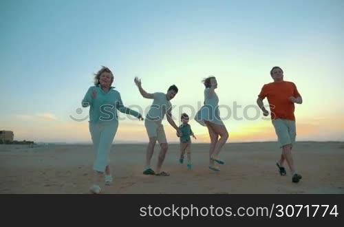 Slow motion of happy family enjoying vacation time. Parents, child and grandparents having fun running and jumping on the beach