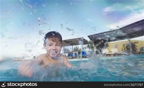Slow motion of happy little child having enjoyable time in the swimming pool. He laughing and splashing water