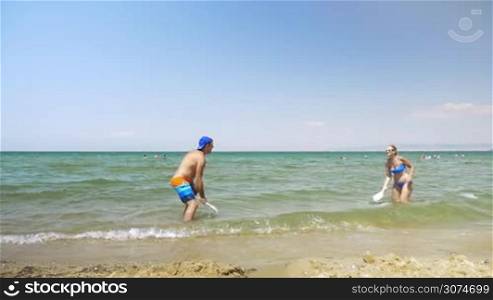 Slow motion of happy man and woman having fun on the beach during summer vacation. They splashing water with ping pong paddles and then playing a game
