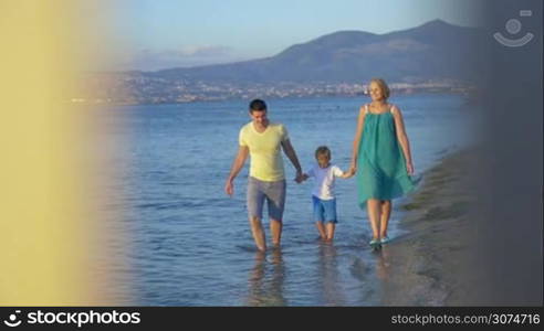 Slow motion of happy mother, father and little son having a walk along the coast with following view to the house model. Owning a family house, villa or vacation home concept