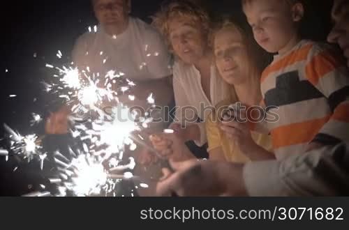 Slow motion of happy young mother and little son playing with Bengal lights at night. Close-up of sparklers