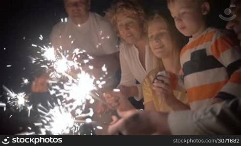 Slow motion of happy young mother and little son playing with Bengal lights at night. Close-up of sparklers