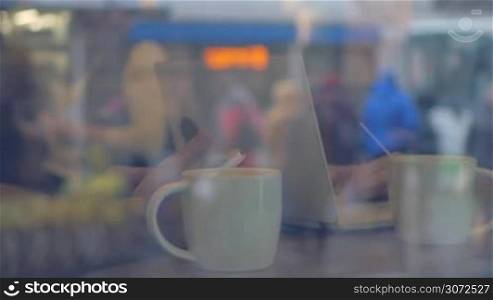 Slow motion of man and woman using smat phone and laptop while having tea in cafe. Reflection of city in the glass