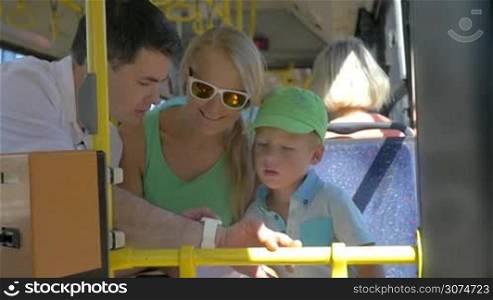 Slow motion of mother, father and little son riding in the city bus. Mom and boy using dads smart watch