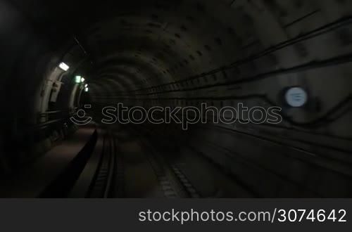 Slow motion of moving forward in dark underground tunnel. Traveling along subway railroad in dim light of wall lanterns
