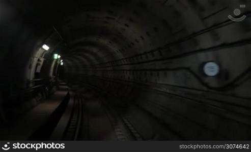 Slow motion of moving forward in dark underground tunnel. Traveling along subway railroad in dim light of wall lanterns