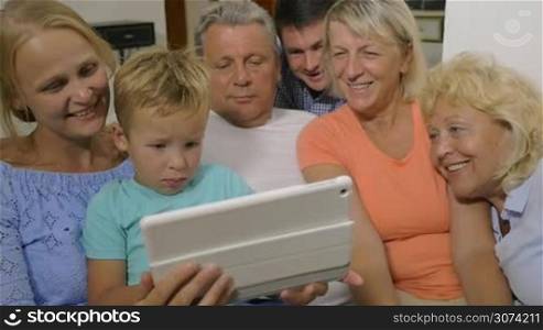 Slow motion of parents, little son and grandparents watching video on tablet computer at home