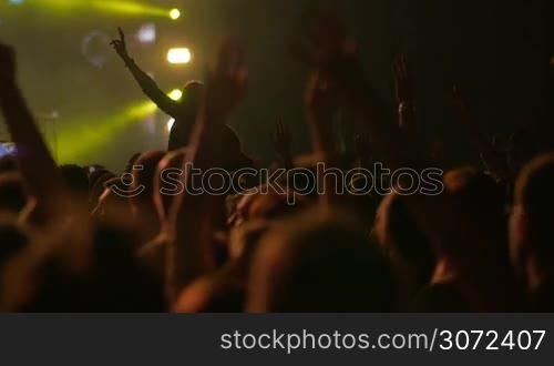 Slow motion of people enjoying favorite music on the concert. They waving hands with a song, video clip is shown on big stage screen