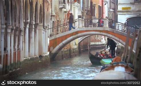 Slow motion of traditional touristic travel on gondola along the canal. Boat sailing under the small bridge