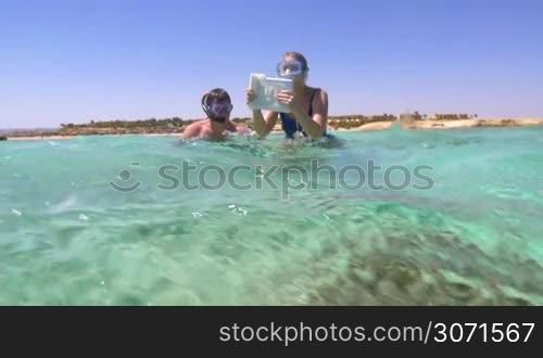 Slow motion of two tourists in snorkels diving with pad to take pictures of underwater scene with coral reef