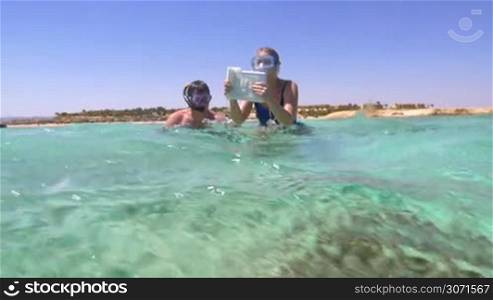 Slow motion of two tourists in snorkels diving with pad to take pictures of underwater scene with coral reef