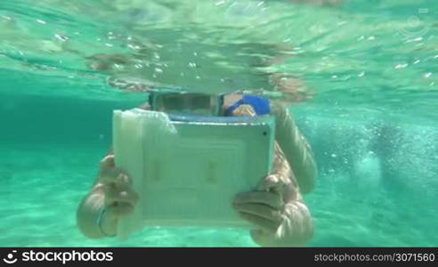 Slow motion of woman in snorkel diving in clear blue water with pad in water-proof case. She trying to make good undersea photo or video