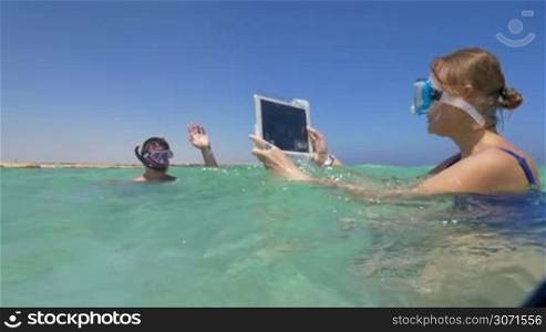 Slow motion of woman taking shots with pad in the sea. She making photo or video of a man in snorkel, tabet computer in water-proof case. Capturing bright moments of summer vacation