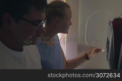 Slow motion of young man and woman traveling by plane. She opening the blind and they both enjoying the view from the illuminator, bright sunlight coming through it