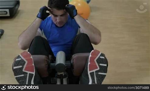 Slow motion of young man doing situps, exercising on special sportive equipment in the gym