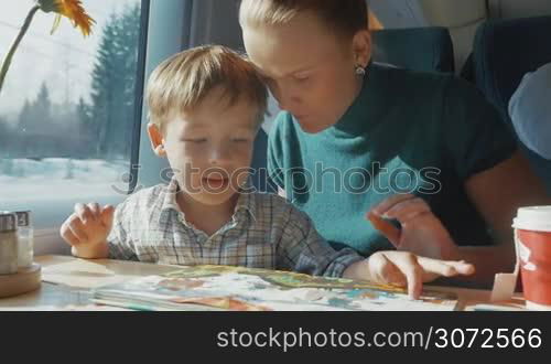Slow motion of young mother and little son looking at pictures in childrens book while traveling by train