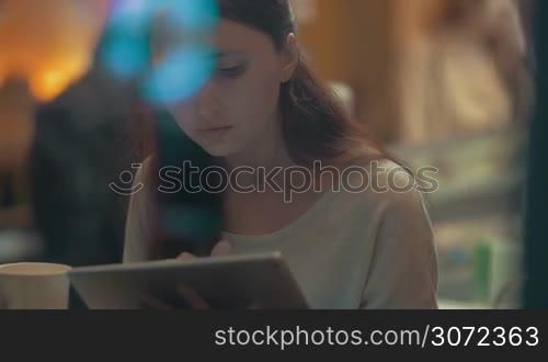 Slow motion of young woman concentrated on using tablet computer in cafe. She browsing the internet or doing something on business