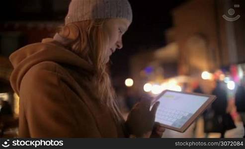 Slow motion of young woman with touch pad in the evening city. She typing and sending message in chat. Blurred street with lights and people in background