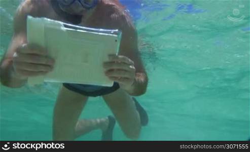 Slow motion shoot of snorkelling young man. He&acute;s shooting an underwater coral reef using tablet PC in waterproof case.