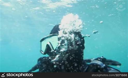 Slow motion shot of a diver breathing under the water. He is exhaling and air bubbles appear around him.