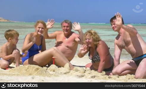 Slow motion shot of a family members sitting on the beach and waving hands merrily.