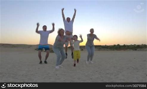 Slow motion shot of a happy family members jumping and raising hands on sunset beach.
