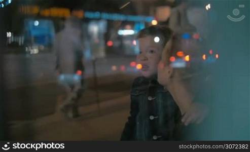 Slow motion shot of a little boy and his mother waiting for a bus, boy is looking at road traffic.