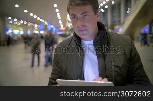 Slow motion shot of a man watching something in tablet PC, he&acute;s standing in air or railway terminal.
