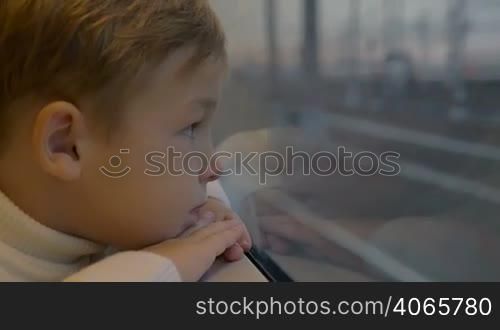 Slow motion shot of a thoughtful boy looking out the train window.