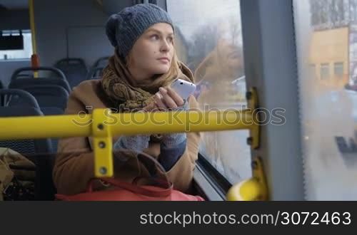 Slow motion shot of a woman riding a bus in dull day, she&acute;s writing something in a smartphone.