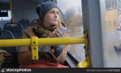 Slow motion shot of a woman riding a bus in dull day, she&acute;s writing something in a smartphone.