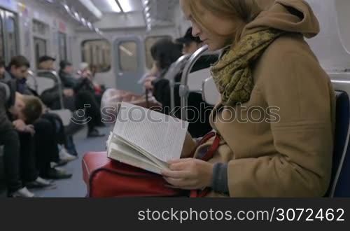 Slow motion shot of a woman sitting in tube train and reading a book.