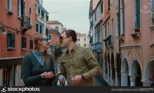 Slow motion shot of a young couple standing outdoor in Venice, Italy wearing Venetian carnival masks. They are kissing, smiling and throwing confetti.