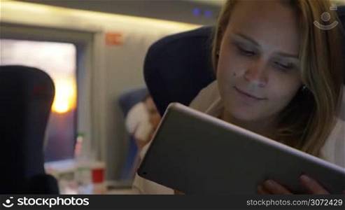 Slow motion shot of a young woman traveling by train and staying in touch with friends using tablet PC on the way.
