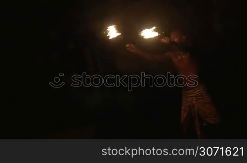 Slow motion shot of an episode of fire show. Dark-skinned artist makes huge fire explosion with two lighting torches.