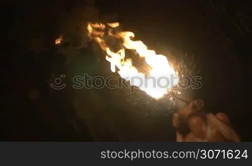 Slow motion shot of an episode of fire show. Dark-skinned fire-breather makes a big explosion of fire.