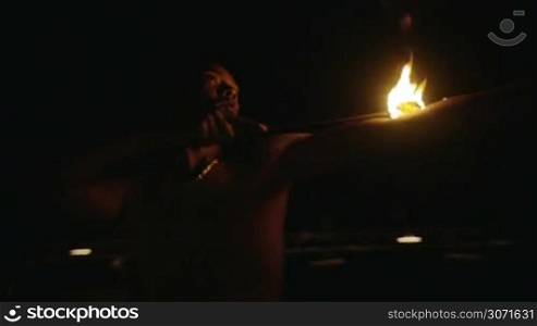 Slow motion shot of an episode of fire show. Dark-skinned artist puts burning torch on his arm and body.