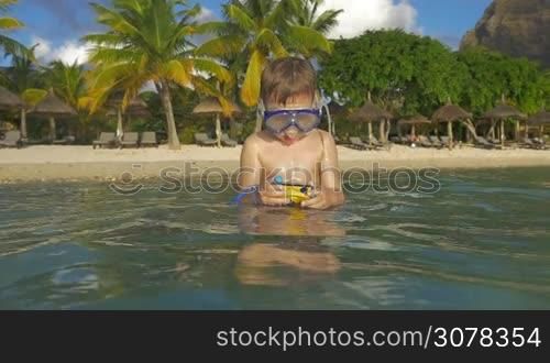 Slow motion shot of child in snorkel bathing in the sea with waterproof camera. He searching for good underwater shots during vacation on tropical resort