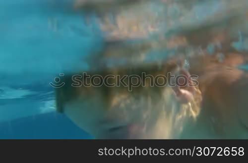 Slow motion shot of parents and son diving in swimming pool and playing under water.