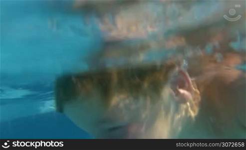 Slow motion shot of parents and son diving in swimming pool and playing under water.