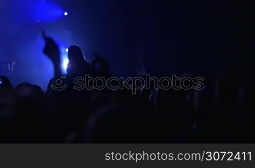 Slow motion shot of people came to the concert. Concert hall is dark, illuminated only with spotlights.