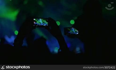 Slow motion shot of people holding smartphones over the heads to shoot the performance on the stage.