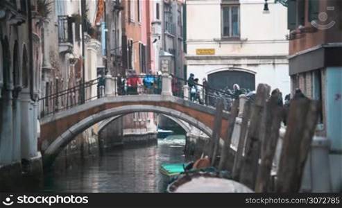 Slow motion shot of people on the bridge over the water canal in Venice, Italy. Locals are crossing it, tourists are standing and taking photos, city birds are flying over people.