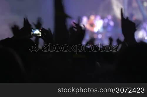 Slow motion shot of people on the musical concert. People are dancing, taking photos, girls are sitting on shoulders of their friends.