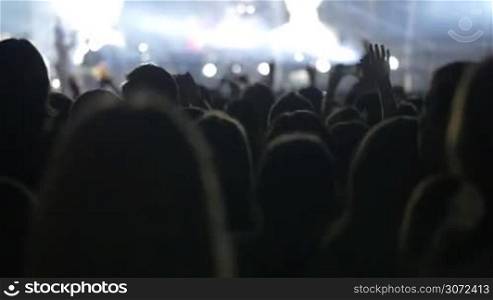 Slow motion shot of people standing in front of the stage and watching the show of a musical band.