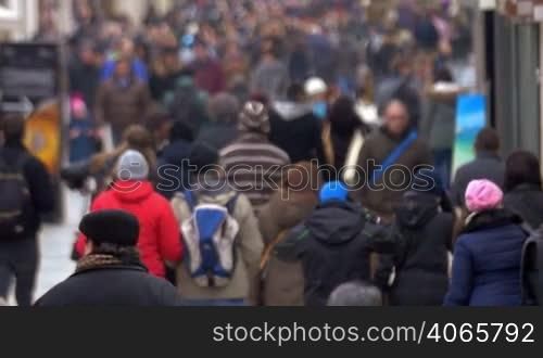 Slow motion shot of people walking along the crowded street in spring or fall. Shot is made with slight defocus.