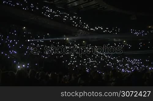 Slow motion shot of stadium stand full with people. They are lighting lamps in the dark.