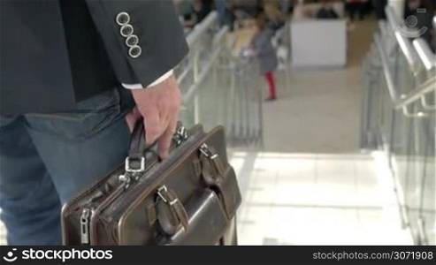 Slow motion, steadicam and close-up shot of a businessman holding leather briefcase going downstairs in trade center