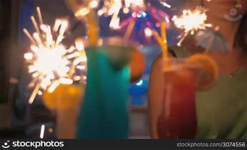 Slow motion steadicam and close-up shot of colorful summer cocktails with sparklers on tray held by young woman