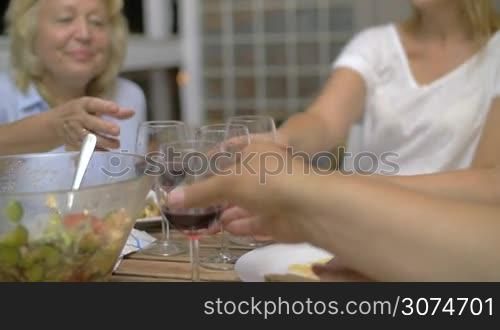 Slow motion steadicam shot of a family clanging glasses with red wine during dinner. Enjoyable evening with close people